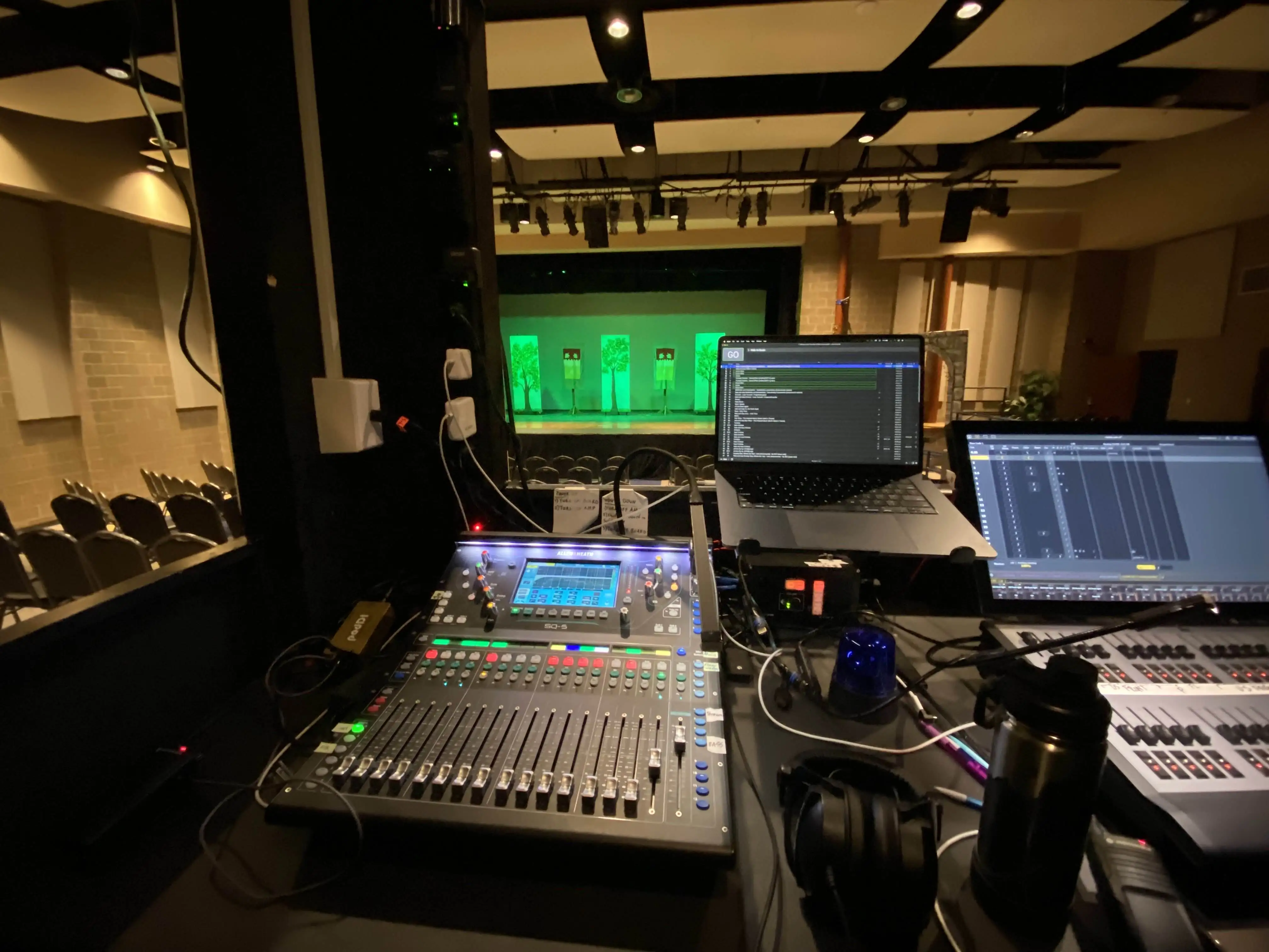A view of a sound board and laptop on a desk, overlooking a stage.